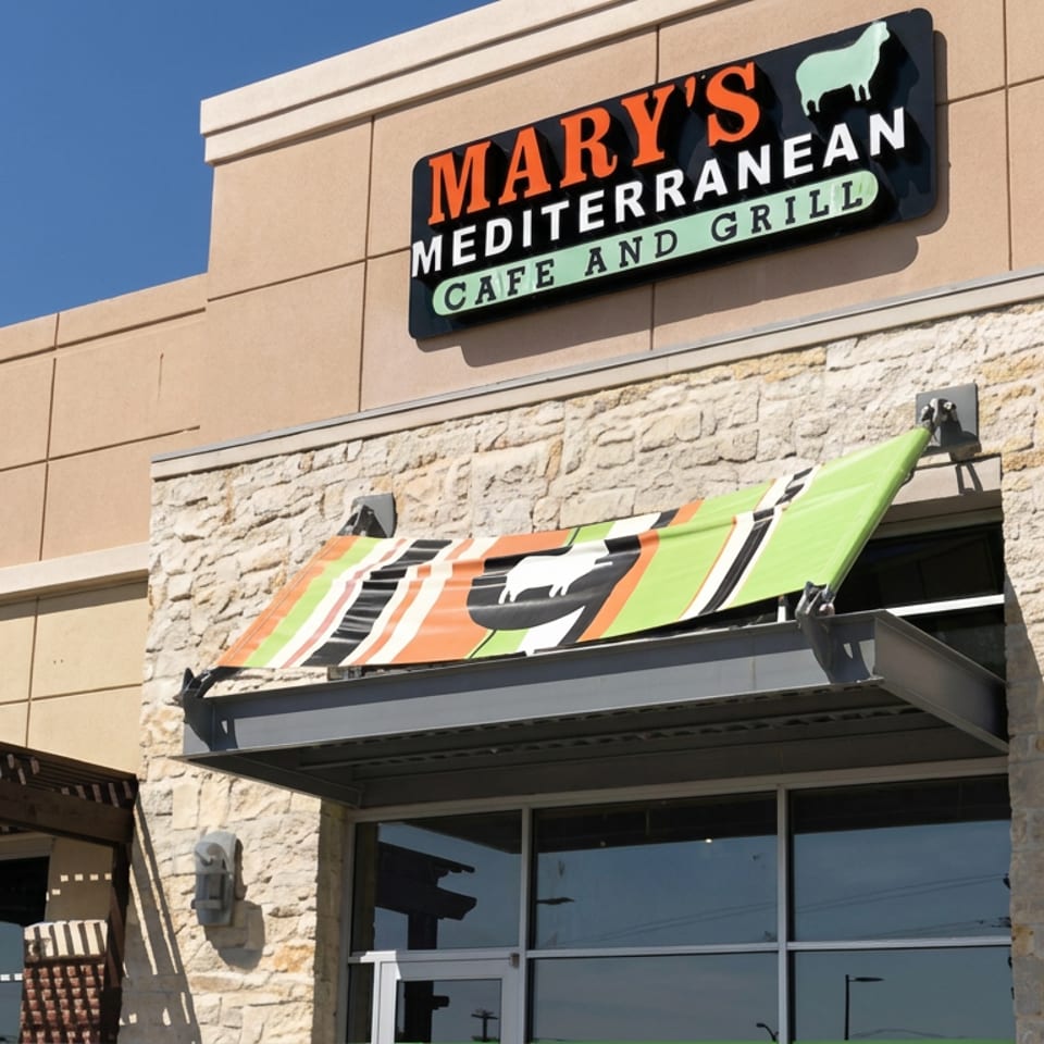 Exterior of Mary's Mediterranean Cafe and Grill, featuring a stone facade, colorful awning, and prominent restaurant sign.