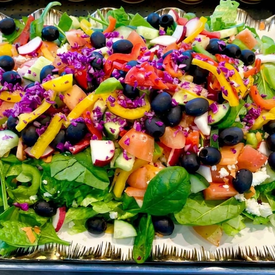 Colorful garden salad with spinach, lettuce, tomatoes, cucumbers, peppers, blueberries, radishes, and purple cabbage on a serving platter.